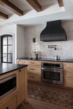 a kitchen with wooden cabinets and black counter tops, an oven hood over the stove