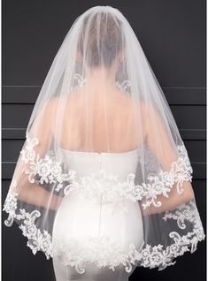 the back of a bride's veil with white flowers and leaves on it, against a black background