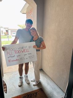 a man and woman standing in front of a door holding a sign