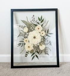 an arrangement of white flowers in a black frame on the floor next to a wall