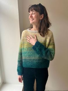 a woman standing in front of a window wearing a green and yellow sweater with stripes