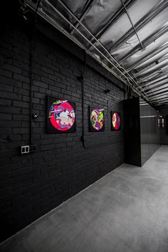 an empty room with black brick walls and paintings on the wall in different shapes, sizes and colors