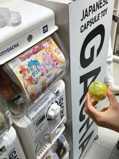 a person holding an item in their hand near a machine with japanese comics on it