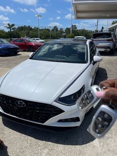 a white car is parked in a lot with other cars and someone holding the keys