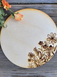 a white plate with flowers on it sitting on a wooden table next to an orange flower