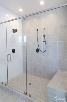 a walk in shower sitting next to a white tiled wall and floor with glass doors