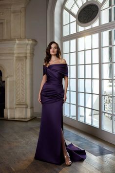 a woman in a long purple dress standing by a window