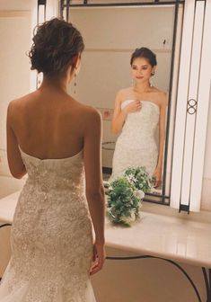 a woman standing in front of a mirror wearing a wedding dress