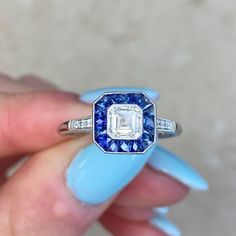 a woman's hand holding an engagement ring with a blue and white diamond in it