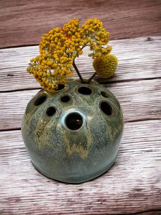 a vase with yellow flowers in it sitting on a wooden table next to a piece of wood