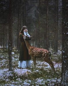 a woman is standing in the woods with a deer