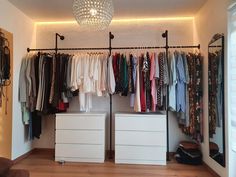 an organized closet with clothes hanging on the rails and two white drawers under a chandelier