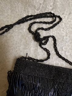 a black beaded purse sitting on top of a white cloth covered floor next to a chain