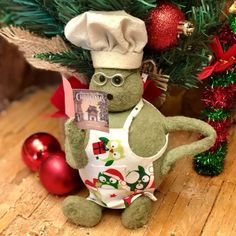 a stuffed animal wearing a chef's hat and apron next to a christmas tree