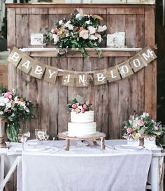 a table topped with a cake and flowers next to a wooden sign that says baby in bloom