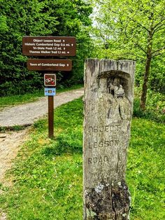 a wooden sign in the middle of a grassy area with trees and grass around it