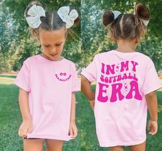 Introducing our Girls Comfort Colors® T-Shirt, a stylish and personalized piece that celebrates her being in Softball Era.. With its unique design and customizability, this shirt is perfect for your little girl to showcase her pride and individuality. The back of the shirt features a large and eye-catching print that boldly states "In my Softball era".  On the front, you'll find a trendy pocket print that adds a cool and fashionable element to the shirt. As an extra personal touch, we offer the Pink Short Sleeve T-shirt With Team Name, Pink Team Spirit T-shirt With Short Sleeves, Pink School Spirit T-shirt With Name Print, Pink School Spirit Tops With Name Print, Pink Short Sleeve Tops With Team Name, Pink T-shirt With Team Name For Cheerleading, Pink Letter Print T-shirt For Cheerleading, Customizable Pink Short Sleeve Shirt, Customizable Playful Pink T-shirt