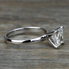 a white gold engagement ring with a princess cut diamond in the center on a wooden surface