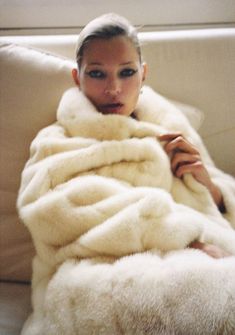 a woman sitting on a couch wrapped in a white fur coat and posing for the camera