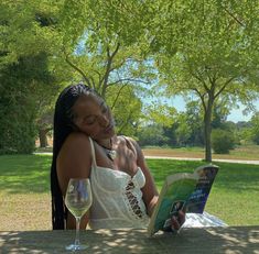 a woman sitting at a table reading a book and holding a wine glass next to her