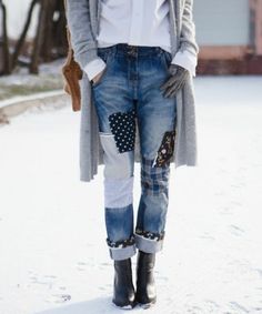 a woman standing in the snow wearing jeans and a cardigan jacket with patches on it