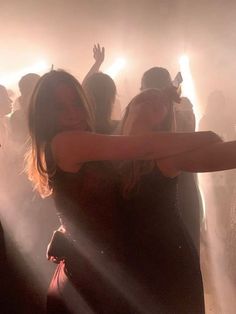 two women in black dresses dancing on a dance floor with their arms outstretched and lights shining behind them