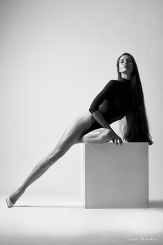 a woman sitting on top of a white box with her legs crossed and long hair in the air