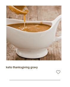 a white bowl filled with gravy on top of a wooden table next to a spoon