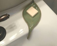 a green leaf shaped soap dish sitting on top of a white sink