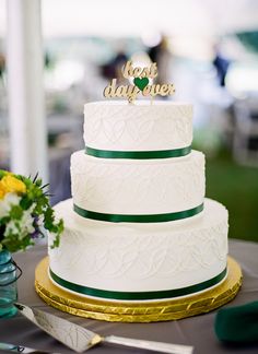 a three tiered white cake sitting on top of a table next to a vase with yellow flowers