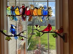 a stained glass bird chandelier hangs in front of a window with an outside view