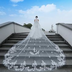 a woman in a wedding dress standing on some stairs with a veil over her head