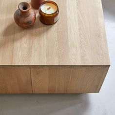 a wooden table with a vase and candle on it, next to a ceramic container