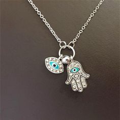 Introducing our Women's Fashion Jewelry Silver or Gold Plated Evil Eye Hamsa Hand Necklace, a stylish and symbolic accessory that combines the protective powers of the Evil Eye and the Hamsa Hand. The pendant of this necklace features a beautifully designed Hamsa Hand, a traditional symbol known for its protective qualities and ability to ward off negative energies. The Hamsa Hand is believed to bring luck, happiness, and blessings to the wearer. At the center of the Hamsa Hand pendant is the Evil Eye, a symbol used for centuries to protect against malevolent forces and to ward off negative influences. The Evil Eye is said to watch over the wearer, deflecting negative energy and bringing good fortune and protection. This necklace is available in either silver or gold plating, allowing you Long Silver Spiritual Charm Necklaces, Spiritual Metal Necklaces With Charms, Spiritual Metal Charm Necklaces With Adjustable Chain, Spiritual Metal Charm Necklace With Adjustable Chain, Evil Eye Symbolic Metal Jewelry, Symbolic Evil Eye Metal Jewelry, Silver Charm Necklaces With Adjustable Chain For Good Luck, Silver Charm Necklace With Evil Eye For Good Luck, Silver Evil Eye Charm Necklace For Good Luck