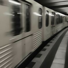 a blurry photo of a subway train passing by in black and white, with people walking on the platform