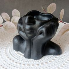 a black vase sitting on top of a table next to white doily with leaves