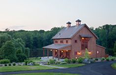 a large red barn sitting in the middle of a lush green field next to trees