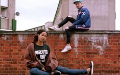 two people sitting on the side of a brick wall