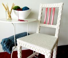 a white table with a bowl of yarn on it and a chair next to it