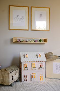 a doll house sitting on top of a rug next to two framed pictures above it