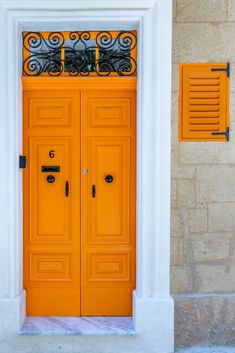 an orange door with iron bars on the top and bottom, in front of a stone building