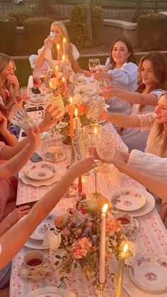 a group of women sitting around a table with plates and glasses on it, all holding candles