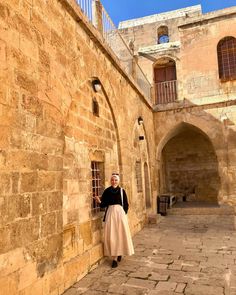 a woman standing in an alley way next to a stone building with arched doorways