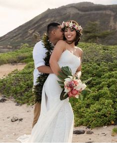 a bride and groom standing on the beach with their arms around each other as they kiss