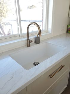 a white kitchen sink sitting under a window next to a counter top with a faucet