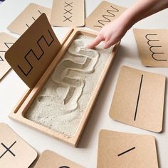 a child is playing with sand in a wooden box and matching numbers on the floor