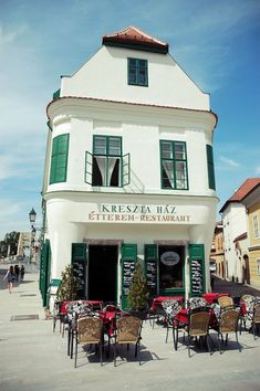 an outdoor restaurant with tables and chairs in front of the building that has green shutters