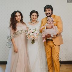 three people standing next to each other with a baby in their arms and holding flowers