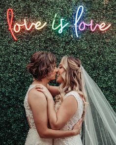 two brides standing in front of a love is love sign