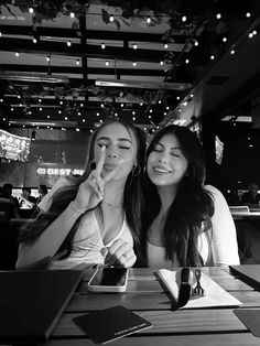 two young women sitting at a table with their fingers up to their lips and looking into the camera